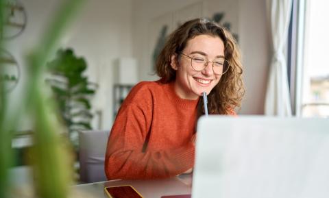 Junge Frau lächelt und sitzt vor einem Laptop.