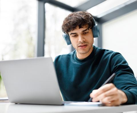Männlicher Student mit Kopfhörer lernt vor einem Laptop