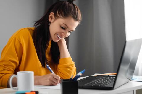 Eine junge Frau sitzt vor einem Laptop und schreibt