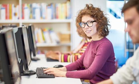 Junge Frau lächelt und sitzt vor einem Laptop.