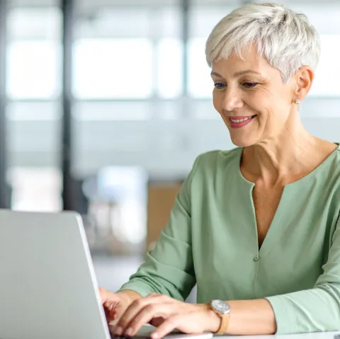 Frau, mittleren Alters, sitzt vor Laptop und tippt