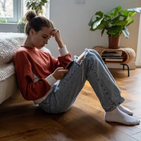 Gesundheitskompetenz bei Jugendlichen, Teenager sitzt am Boden und schaut in ihr Handy