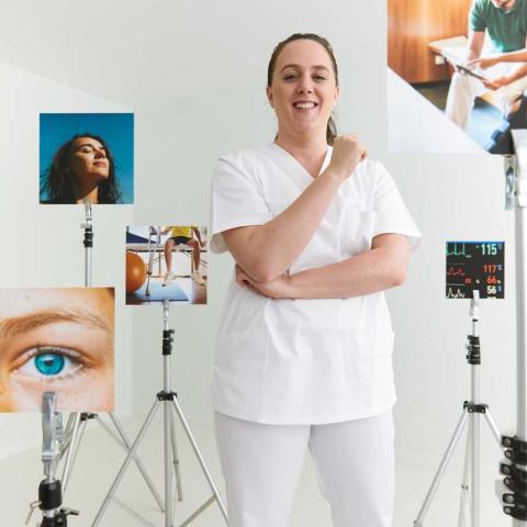 Pflegefachfrau steht vor verschiedenen Bildern und lächelt in Kamera