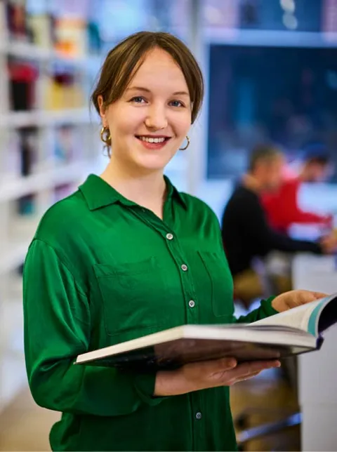 Studentin liest Buch in Bibliothek