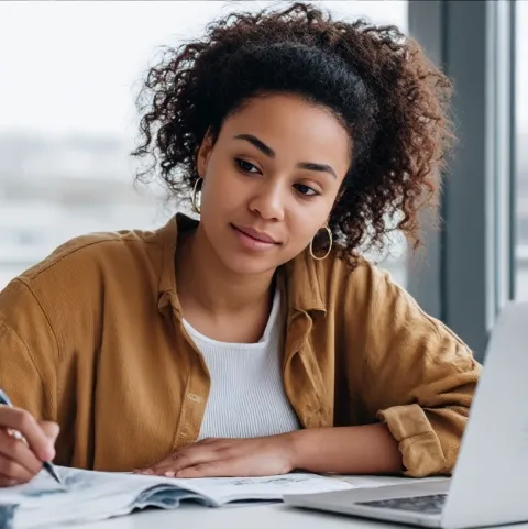 Junge Frau lächelt und sitzt vor einem Laptop und schreibt etwas.