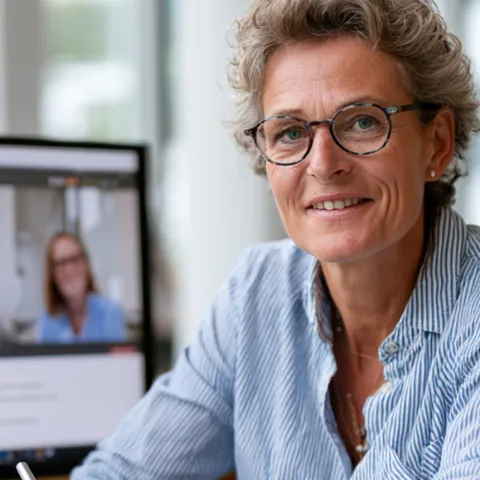 Frau, mittleres Alter, sitzt vor einem Laptop mit Teilnehmern an Webinar